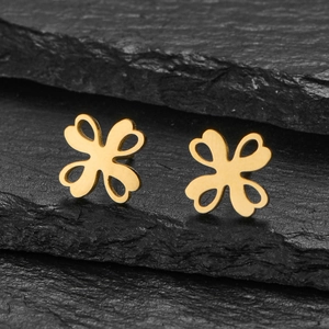 Macro detail of gold clover stud earrings with heart cutouts on a textured stone surface
