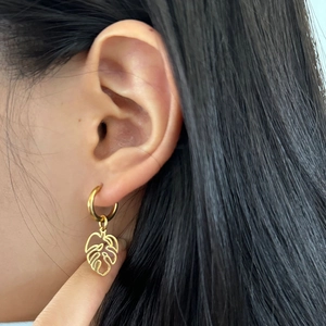 Vue macro de boucles d'oreilles pendantes feuille de monstera dorée au design épuré
