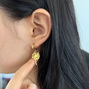 Détail d'une boucle d'oreille fleur en or portée par un mannequin pour montrer le style