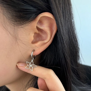 Gros plan d'une boucle d'oreille en acier argenté avec pendentif fleur porté par un mannequin