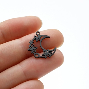 Detailed view of black moon flower cutout charms held in hand for size comparison