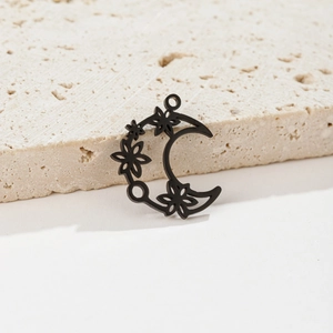 Detailed close-up of a matte black moon pendant with floral cutouts on a stone surface
