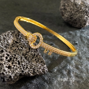 Luxury gold-plated key bangle with cubic zirconia on a minimalist black stone background