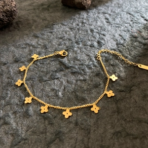 Elegant gold plated stainless steel clover bracelet on a textured dark volcanic rock base
