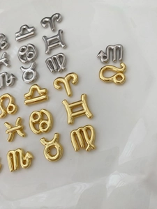 Polished gold and silver zodiac charm pendants displayed on a white ceramic tray