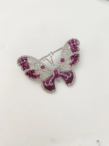 Detailed close-up of a silver butterfly brooch with pink and white gemstones on white background