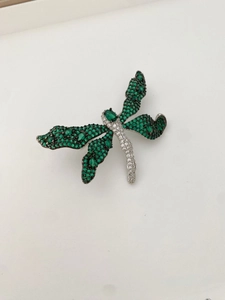 Macro shot of dragonfly brooch with emerald crystals and white diamond pavé details