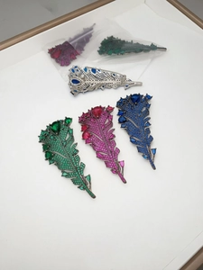 Detailed view of feather leaf brooches featuring emerald crystals and pin back clasp