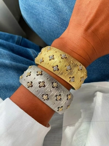 Dettaglio di bracciali in metallo spazzolato oro e argento con fiori di zirconi
