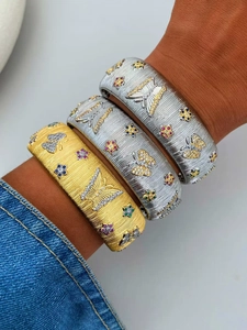 Detail of brushed gold and silver cuff bracelets with colorful butterfly and floral stones