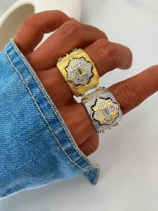 Close-up of wide brushed gold and silver rings featuring floral cz clusters and baguette stones