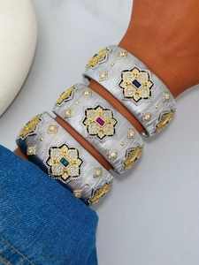 Detailed macro shot of brushed silver bangles with gold floral accents and colored gemstones