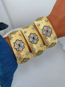 Dettaglio di bracciali in oro spazzolato con motivi floreali e gemme preziose colorate