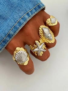 Detail of 18k two-tone gold ocean rings featuring starfish and seashell designs on hand