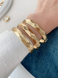 Close-up of golden geometric hammered bangles with hinge closure on a person's wrist