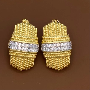 Détail de boucles d'oreilles géométriques dorées avec texture tissée et zircons