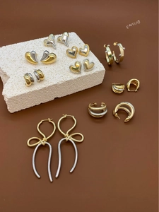 Selection of mixed metal bow and geometric earrings displayed on white stone pedestals