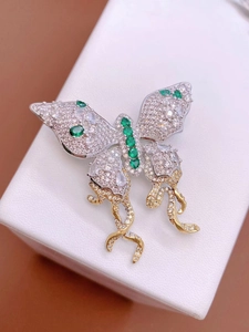 Macro-opname van zilveren vlinderbroche met groene edelstenen en gouden franjes