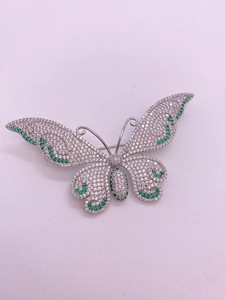 Close-up of pavé set white zircon and green gemstones on silver butterfly brooch