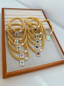 Detail of beaded gold bracelets with micro-pave cross charms and white pearls on tray