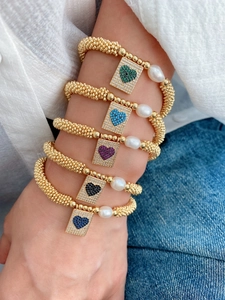 Close-up of five layered gold beaded bracelets with colorful zircon heart charms and pearls
