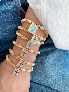 Close-up of stacked gold beaded bracelets with colorful cross pendants and pearls