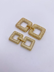 Macro detail of gold-plated square interlocking sweater chain clasps with micro-pave zircons
