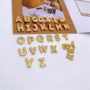 Makroaufnahme von 26 vergoldeten Buchstaben-Anhängern mit funkelnden Kristallen für Schmuck