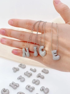 Detail van zilverkleurige alfabet hangers met glanzende zirkonia stenen op de hand