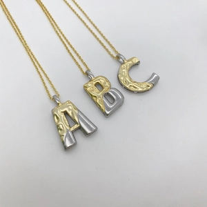 Detail der zweifarbigen ABC-Alphabet-Anhänger mit gehämmerter Metalltextur in Gold und Silber