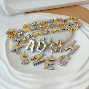 Zweifarbige Buchstaben-Anhänger mit Hammerschlag-Textur auf weißem Tablett für DIY