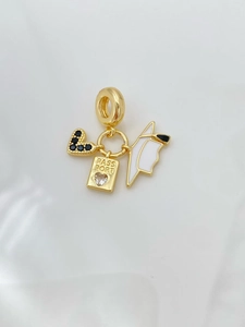 Macro detail of passport charm with black heart and white enamel wing on gold necklace