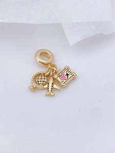 Macro shot of gold globe and airplane charms with pink heart on white fabric