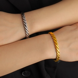 Polierte goldene und silberne gedrehte Armreifen am Handgelenk eines Models mit schwarzem Anzug
