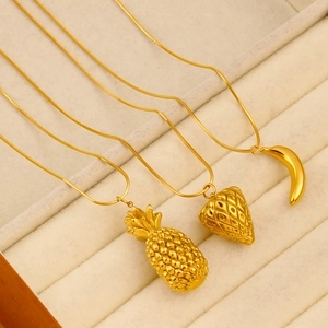 Detailed macro view of gold pineapple, strawberry, and banana fruit pendant necklaces