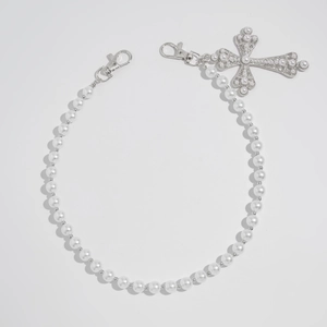 Detailed macro view of a white pearl pants chain with a large ornate cross pendant and clasps