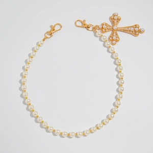 Macro shot of gold cross pendant with pearls and layered waist chain for jeans