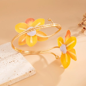 Detailopname van gele stoffen bloemen op een spiraalvormige goudkleurige metalen armband