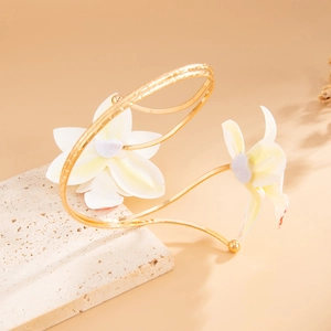 Detail van een elegante gouden armmanchet met witte zijden bloemen en matte texturen
