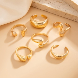 Detail of six minimalist gold teardrop and wavy adjustable rings on a stone display