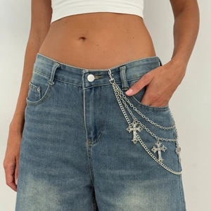 Close-up of multilayer silver cross pendant waist chain on denim jeans with punk style