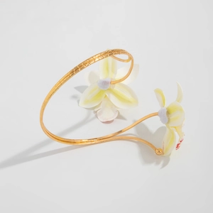 Detail van een gouden bloemenarmband met realistische frangipani-bloemen en metaaltextuur