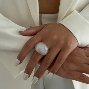 Macro shot of chunky white resin ring with pearlescent finish on model with white blazer