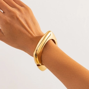 Close-up of a wide polished gold rectangular metal bracelet with hinge closure