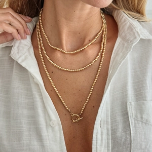 Detail van een gelaagde gouden parelketting met een stijlvolle OT-sluiting op een model
