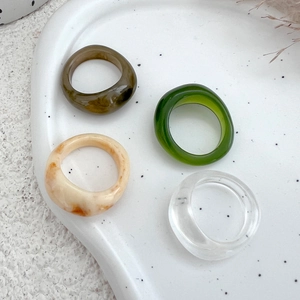 Detail of four colorful acrylic resin rings on a white ceramic tray in minimalist style