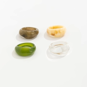 Detail of four acrylic resin rings in marble brown, cream, green and transparent finishes
