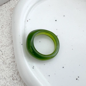 Macro shot of dark green translucent resin ring on minimalist white ceramic tray