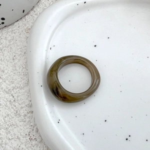 Detailed macro view of olive green marble resin ring on a white ceramic tray