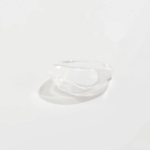 Macro shot of minimalist clear acrylic resin ring with irregular wavy lines on white surface